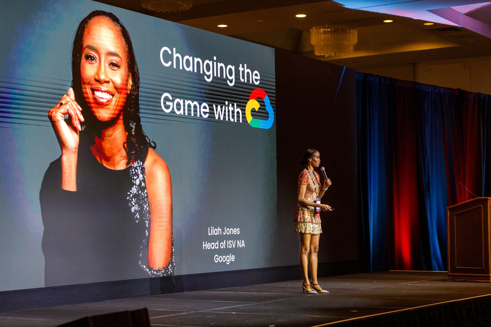 Speaker on stage beside a giant screen showing her portrait