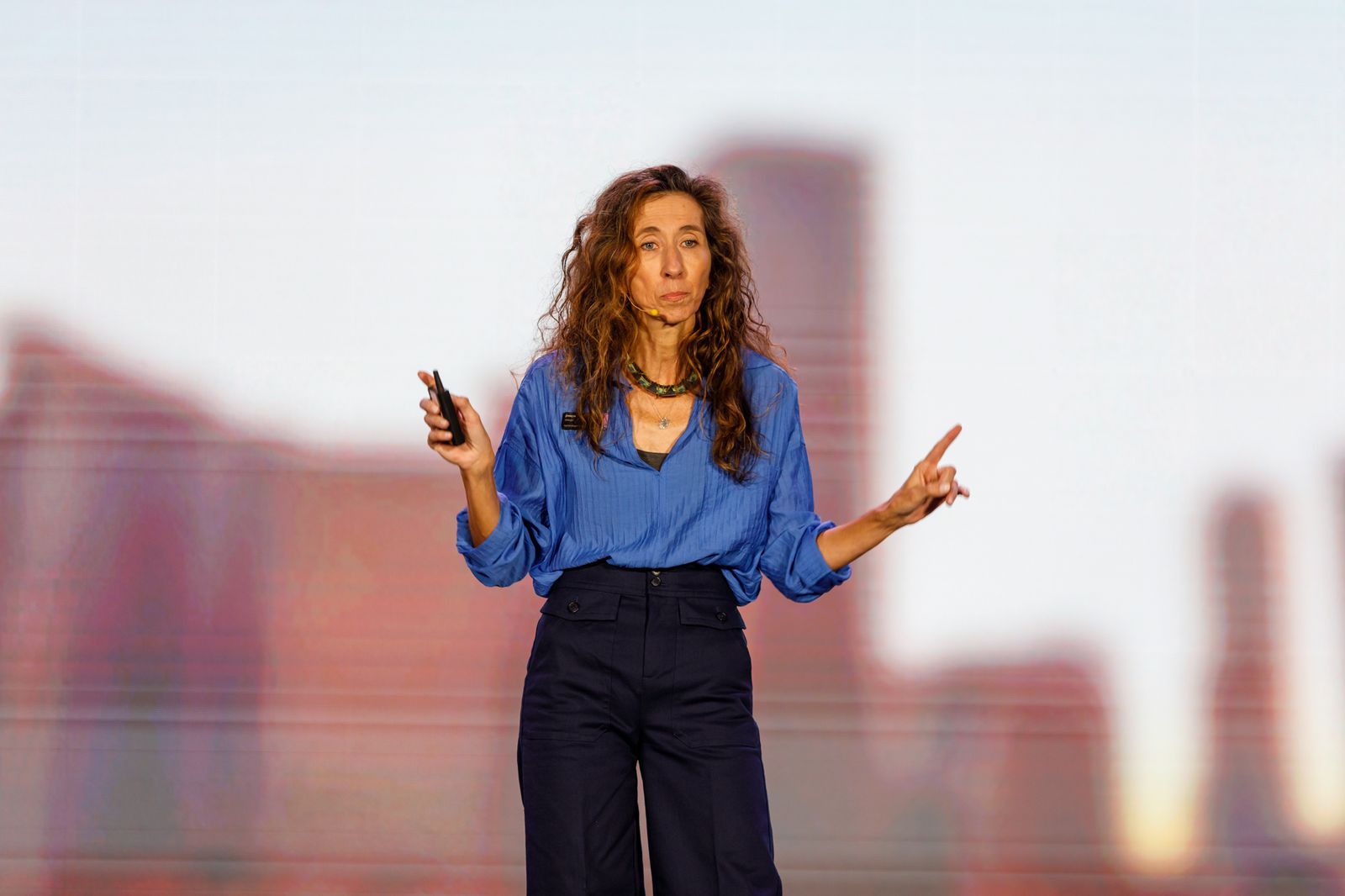 Keynote speaker gesturing on stage in front of a city skyline screen